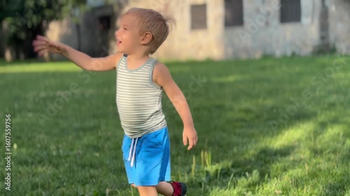 Smiling toddler walking on green grass near stone wall

