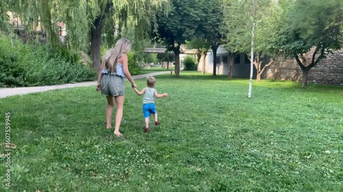 Mother and child walking hand in hand on green grass

