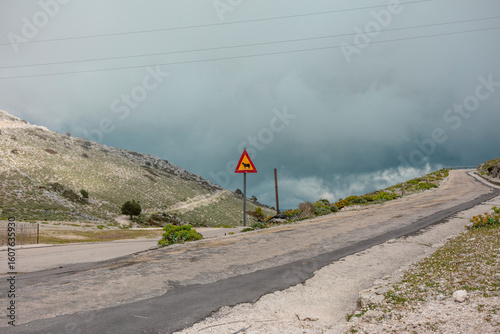 Mountain road with steep grade warning sign indicating challenging driving conditions ahead.