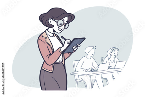 A smiling female teacher wearing glasses and a cardigan writes notes while observing students at desks with laptops in a classroom