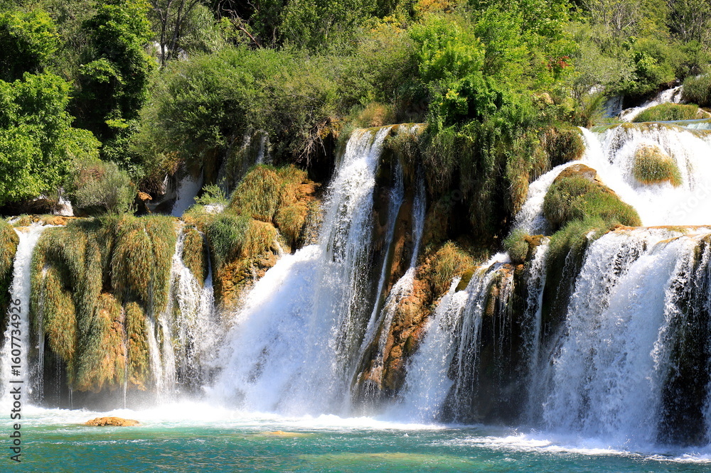 Obraz premium A cascade waterfall among large stones in Krka Park, Croatia, The best big beautiful Croatian waterfalls, mountains and nature.