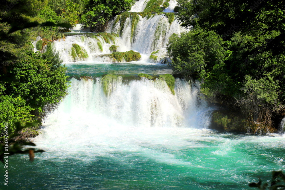 Fototapeta premium A cascade waterfall among large stones in Krka Park, Croatia, The best big beautiful Croatian waterfalls, mountains and nature.