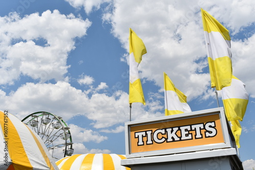 Carnival ticket booth with Ferris wheel in background.