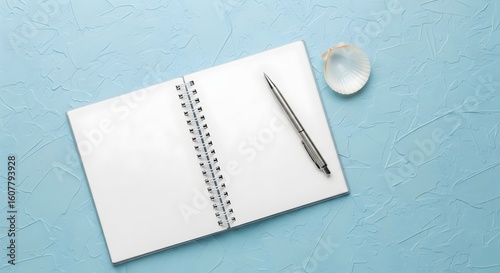 Open Notebook with Pen and Seashell on Textured Blue Background.

