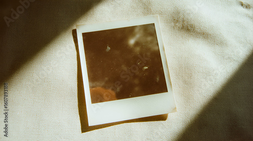 A single blank instant photo frame lies on a soft linen surface, bathed in warm sunlight, evoking a sense of nostalgia and lost memories.
