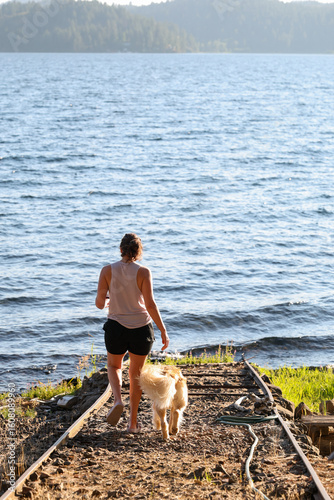 A woman plays with her golden retriever at a lake with fresh water. The dog and the lady are having fun in the summer outside. 