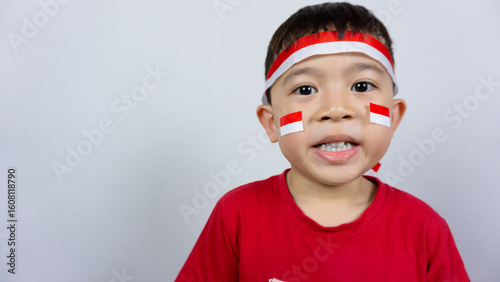 Close-up portrait of an Asian boy wearing a red top and an Indonesian flag ribbon on his forehead and a sticker on his face, isolated on a white background. Indonesian Independence Day concept