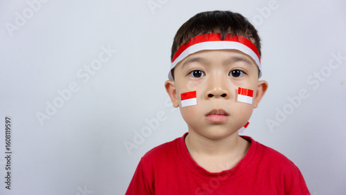 Close-up portrait of an Asian boy wearing a red top and an Indonesian flag ribbon on his forehead and a sticker on his face, isolated on a white background. Indonesian Independence Day concept