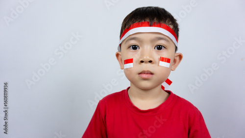 Close-up portrait of an Asian boy wearing a red top and an Indonesian flag ribbon on his forehead and a sticker on his face, isolated on a white background. Indonesian Independence Day concept