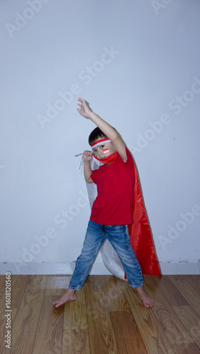Asian boy wearing a red top and blue jeans standing with the Indonesian flag behind his shoulder like a superhero. Indonesian Independence Day concept