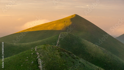 Rolling green hills bathed in golden sunlight create a serene landscape, showcasing natural beauty and tranquility in a peaceful outdoor setting with soft clouds above