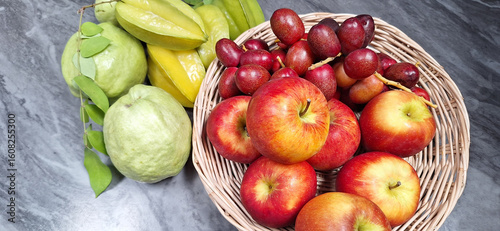 Apples, starfruits, dates, guavas in a white wooden basket on a marble table.