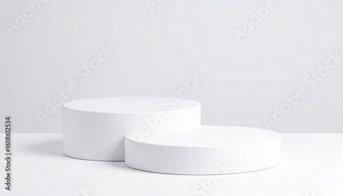 Two white cylindrical platforms in staggered heights on a white surface—evoking minimal structure, layered elevation, and sculptural design harmony.