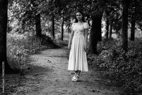 Portrait of a young beautiful dark-haired girl in a dress in the forest. Vintage black and white photo.