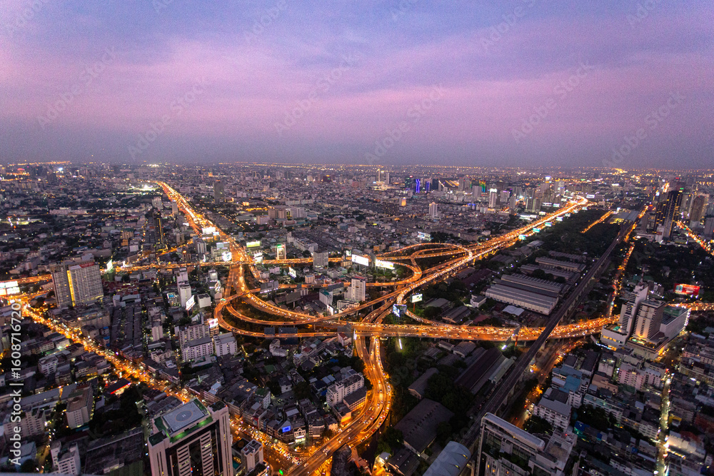 Obraz premium Aerial view of Bangkok, Thailand at twilight, showcasing a vibrant cityscape with illuminated highways, modern buildings, and a glowing purple-pink sky. Captured using landscape photography