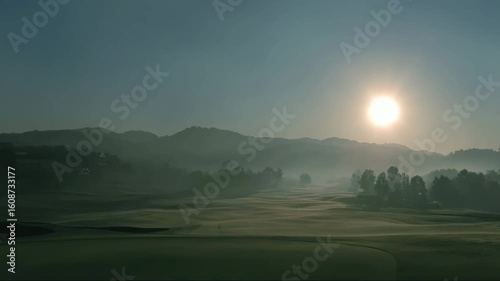 Sunrise over misty golf course with mountains in background  