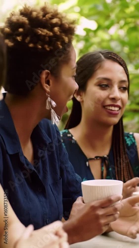 Two to three diverse women, late 20s-early 40s, in joyful, lively conversation at a sun-drenched outdoor cafe with lush green foliage and golden light, holding minimalist coffee cups. concept of joy