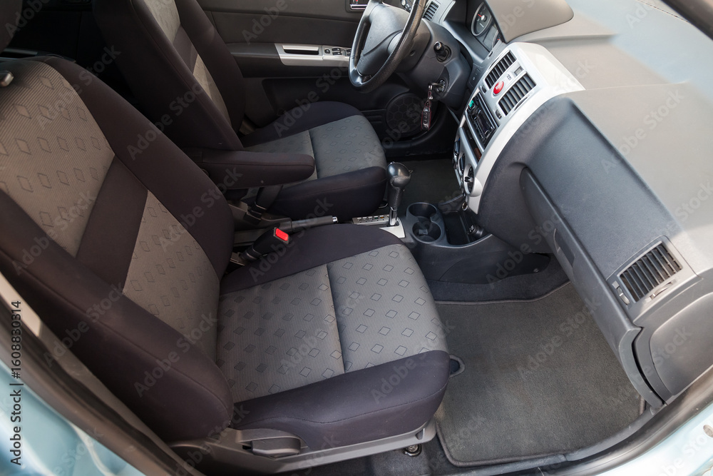 Fototapeta premium Comfortable front seats inside the car: the driver and passenger, tied with black fabric trim, modern interior design, the steering wheel covered and a luxurious center console.