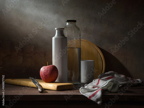 A laconic still life with an apple, a vase, and a bottle of water on a dark background