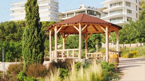 Wallpaper Mural Open wooden gazebo made of light timber with brown tile roof in peaceful public park of Varkiza, Athens, Greece. Surrounded by trees, shrubs, grass, and Nassella tenuissima. No people. Torontodigital.ca