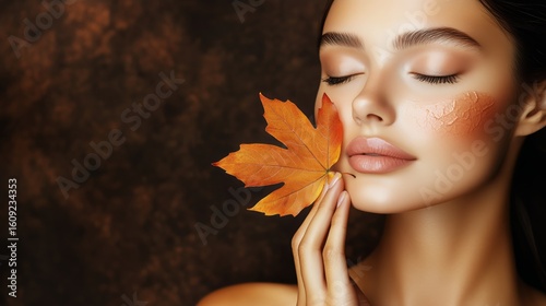 Woman Holds Autumn Leaf Near Face in Natural Lighting With Soft Brown Backgro...
