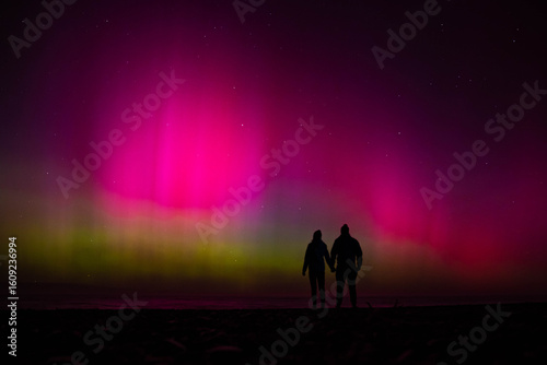 Bild auf Leinwand Silhouette of couple holding hands and gazing at sky lit up by vibrant pink and