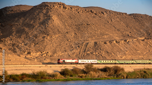 Foto Train traveling between the Nile River and a desert mountain near Aswan, Egypt - a stunning landscape of water and rugged terrain