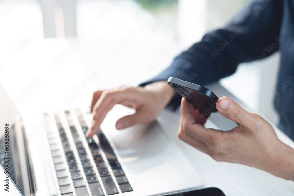 Fototapeta premium Business woman using smartphone and working on laptop computer with digital tablet on office table. Businesswoman surfing the internet, web browsing via laptop and searching the information, closeup