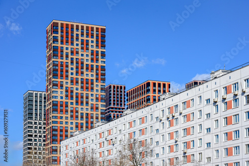 Modern high-rise residential buildings and older apartment block under clear blue sky. Urban contrast of contemporary architecture and traditional housing. Real estate and city development concept.