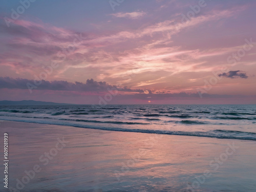 Pink purple sunset over ocean waves and sandy beach image