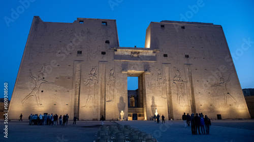 Temple of Edfu illuminated at dawn - golden lights highlight the ancient structure as the sky transitions from night to day in Edfu, Egypt.