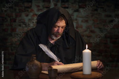 Fotografija A man in monk's clothing writes on a scroll by candlelight.