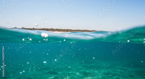 Stunning over-under photograph of a clear turquoise sea with underwater bubbles and a distant green island.
