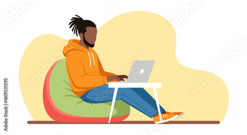 Young Black man working on laptop from beanbag chair, ideal for website or blog illustrating remote work, freelance, or comfortable workspace.