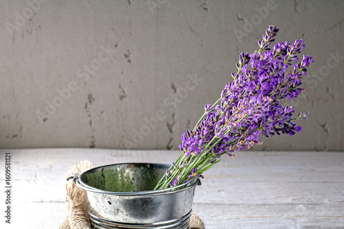 Vibrant lavender bouquet displayed in a metal bucket with rustic plaster wall