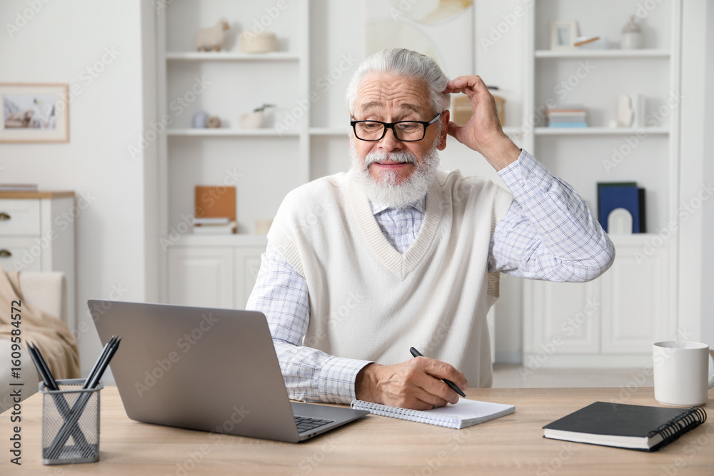 Senior man taking notes while learning online at desk indoors. Self-study Senior man taking notes while learning online at desk indoors. Self-study