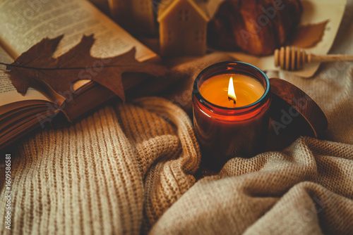 Tableau sur toile Burning amber candle with an open book, autumn leaf, croissant, and cozy knitted textures
