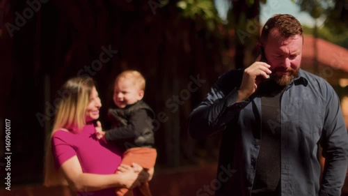 Father Talking on Smartphone While Mother Holding Crying Baby Outdoors
