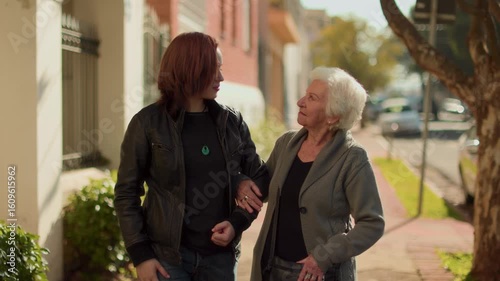Young Woman Walking with Elderly Woman Outdoors on a Sidewalk
