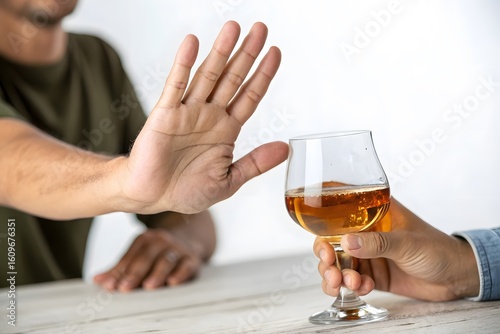 Person refusing alcohol with hand gesture and a glass of liquor on a white wooden table top