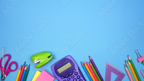 Colorful school supplies moving bottom border. Top view stop motion loop video over a blue background. Back to school concept.
