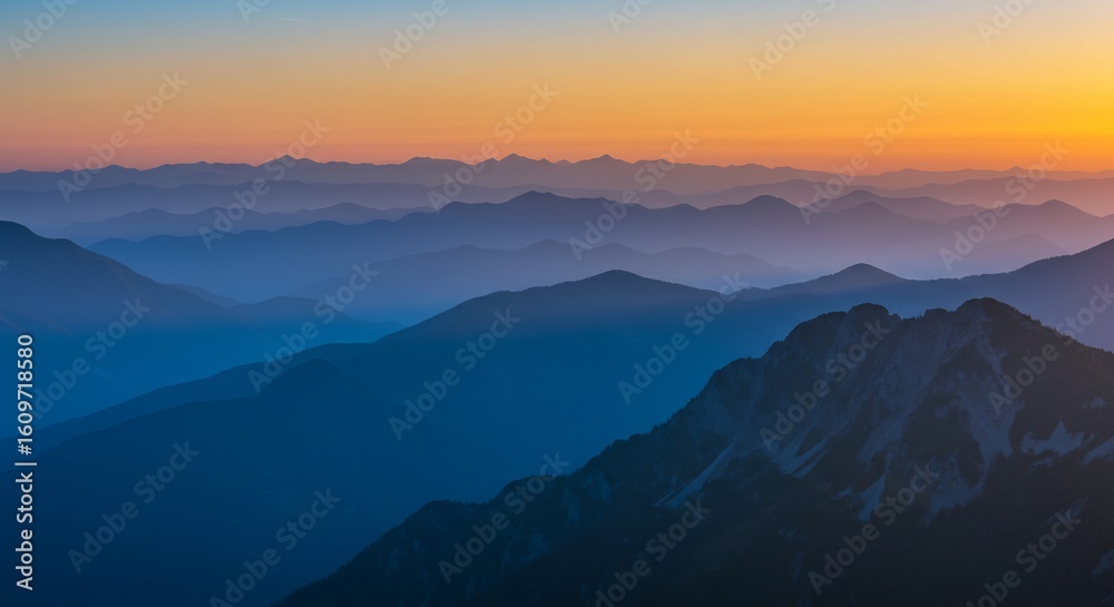 Obraz premium Layered Blue Mountain Range at Sunset with Orange Sky