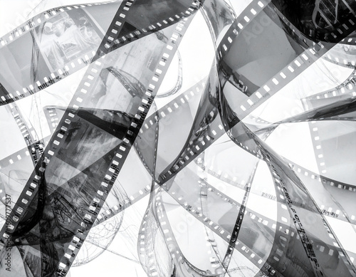Abstract tangle of processed 35mm film strips in black and white, showing sprocket holes and glimpses of frames. Perfect for retro or photographic backgrounds.