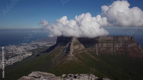Aerial video captures a stunning landscape with clouds enveloping a mountain peak, offering a breathtaking bird's-eye view of the city and coast.
