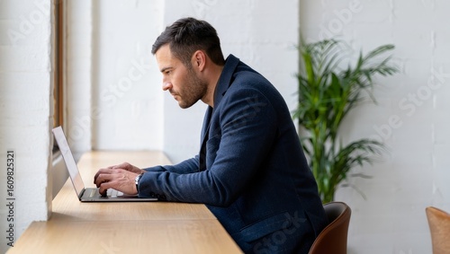 Man working on laptop in modern office, business professional typing on computer desk