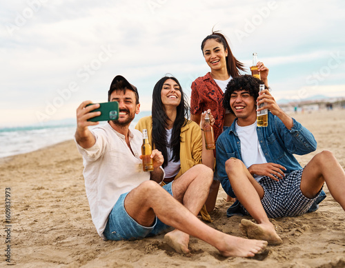 Group of young cheerful people having fun and drinking beer, taking selfie photo with mobile phone camera at the party on the beach looking happy, Enjoying youth and freedom concept
