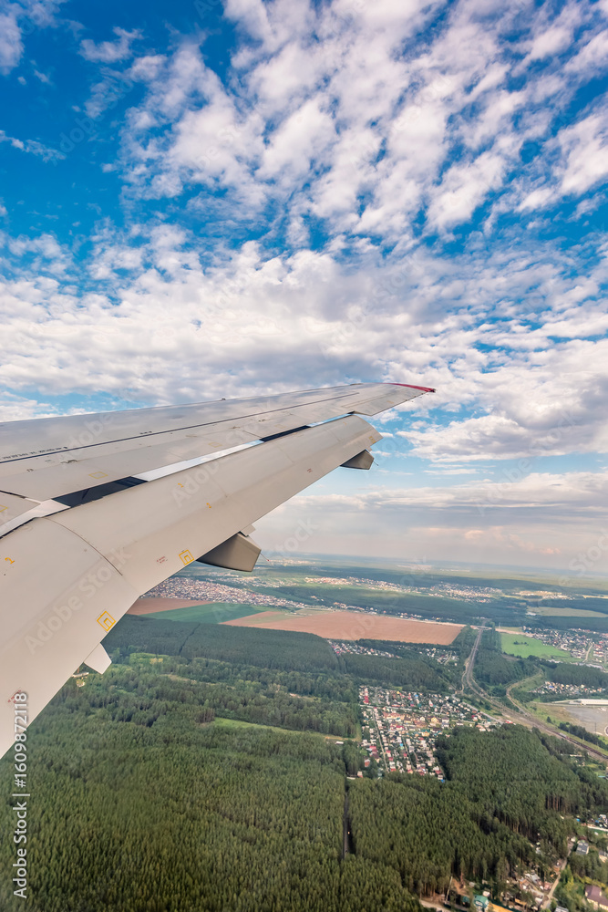 Fototapeta premium View of airplane wing, blue skies and green land during landing. Airplane window view.