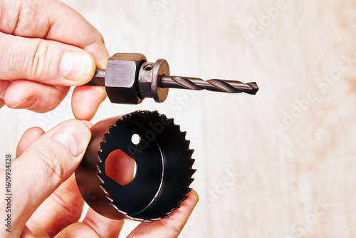 Mandrel with pilot drill bit held in one hand hole saw with teeth held in other hand unassembled woodcutting tool components visible from side angle.