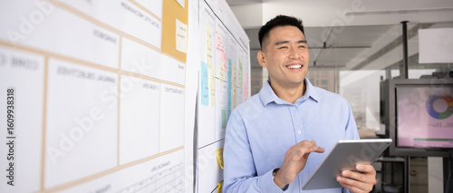 Man stands next to white board covered with sticky notes hold tablet looking up data, statistics, researching stare away with contented smile. Strategizing, planning, innovative tech, horizontal photo