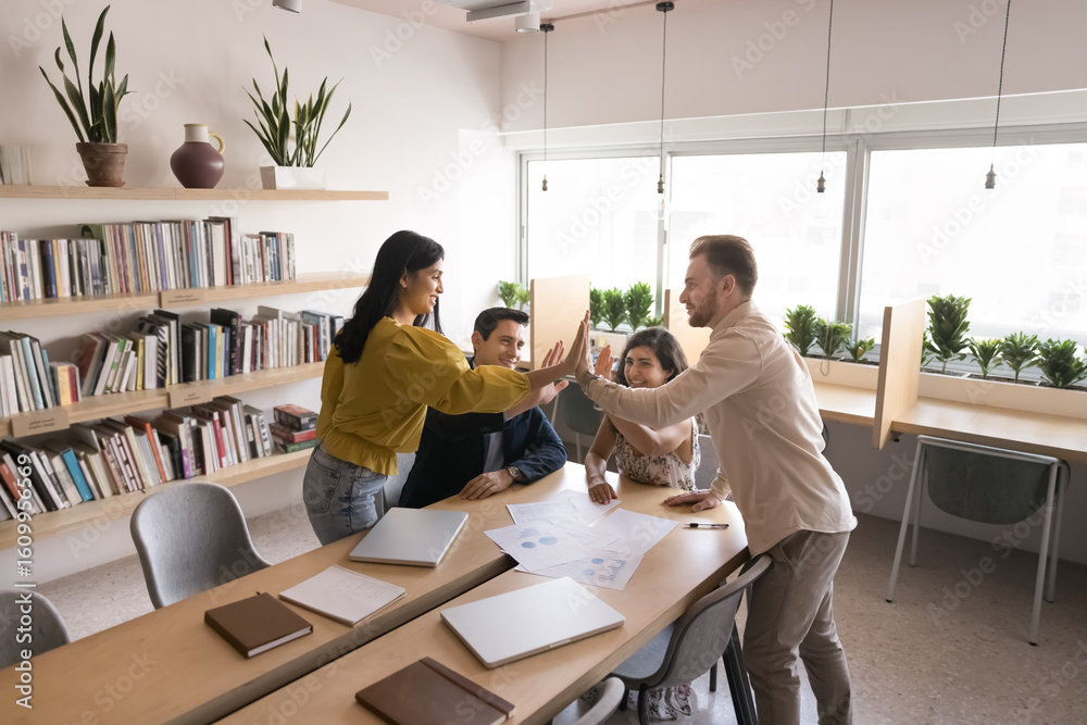Obraz premium Happy businesspeople, staff members team giving high five gesture, gathered in modern boardroom, express support, showing unity, celebrate joint achievements, sales or career growth. Business success